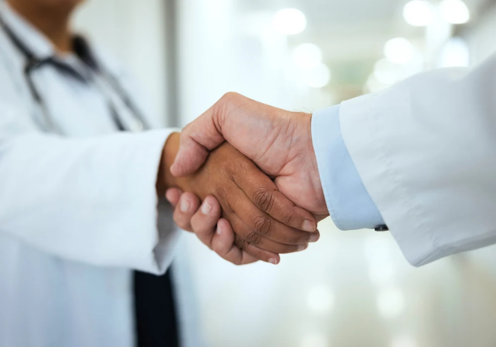 Two doctors shaking hands in hospital corridor, symbolising collaboration and partnership. 
