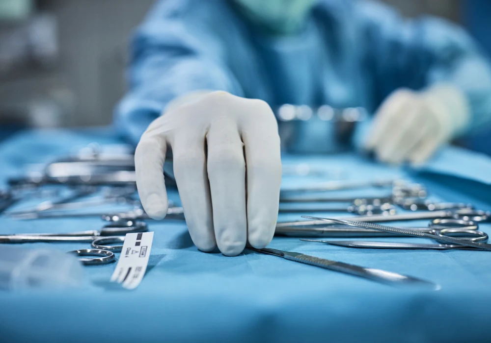 Surgeon in operating room reaching for surgical instruments on sterile table during procedure 
