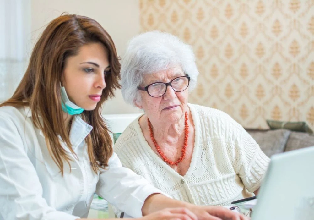 Caregiver helps an older resident use a laptop during cybersecurity and digital literacy training in senior care. 
