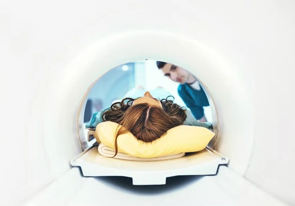 Patient lying inside MRI scanner, viewed from the gantry opening, with a healthcare professional providing reassurance before imaging. 