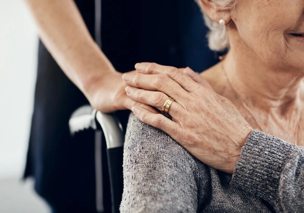 Elder care and reassurance shown by a caregiver’s hand on the shoulder. 