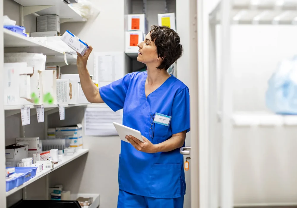 Nurse managing medical supplies and inventory using a digital tablet in a hospital storage room.
