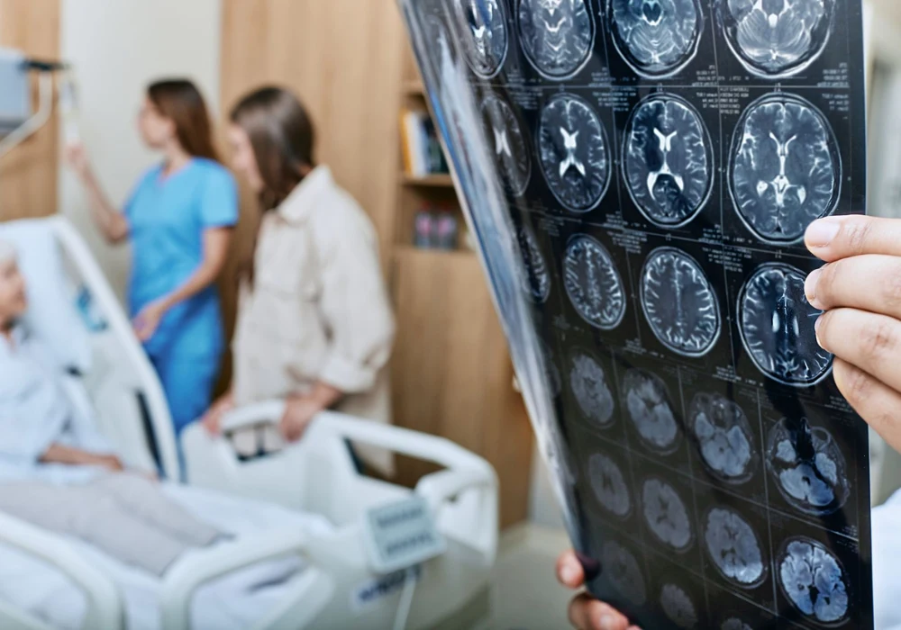 Clinician reviews brain MRI scans beside a hospitalised patient.