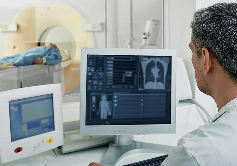 Radiology technician monitoring a patient undergoing a CT scan from a control room.