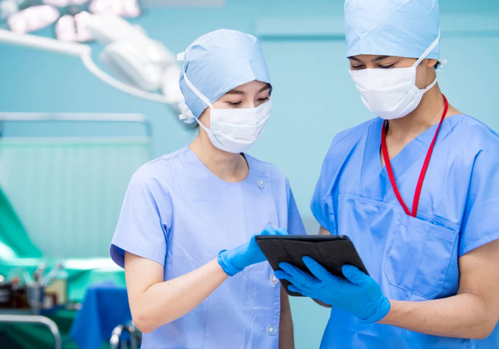 Two surgical staff in scrubs reviewing information on a tablet.