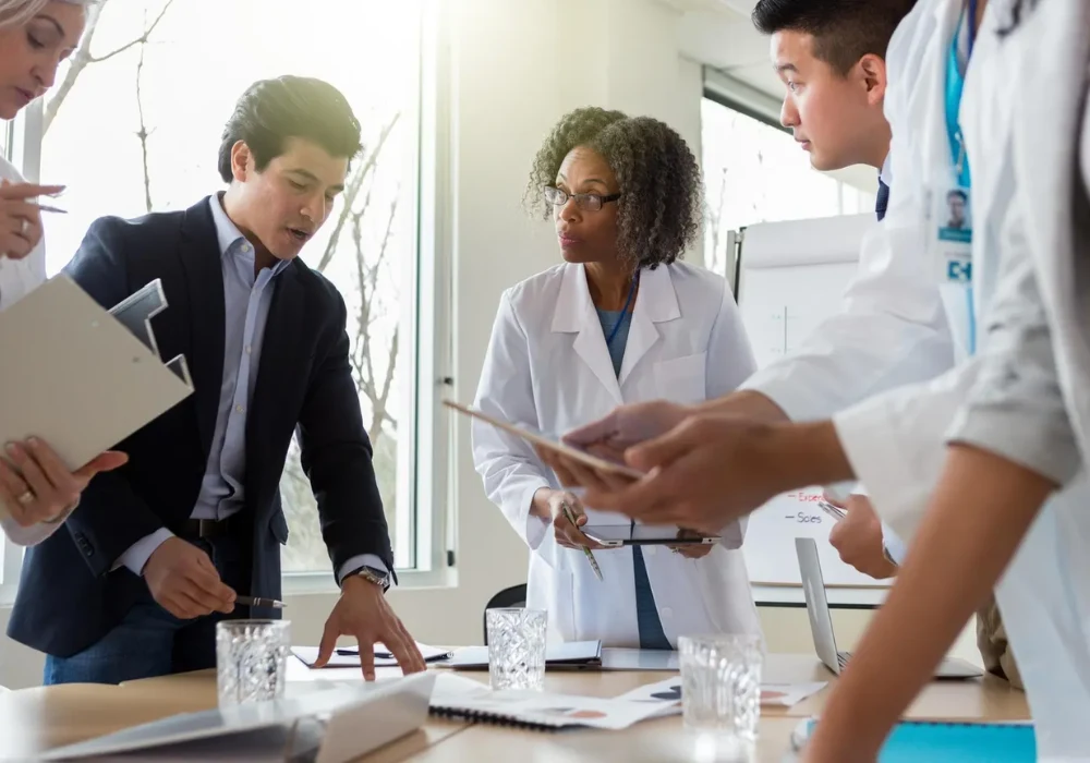 Multidisciplinary healthcare team reviewing documents in a meeting, illustrating collaborative decision-making, care coordination and integration of clinical and managerial perspectives in healthcare delivery.