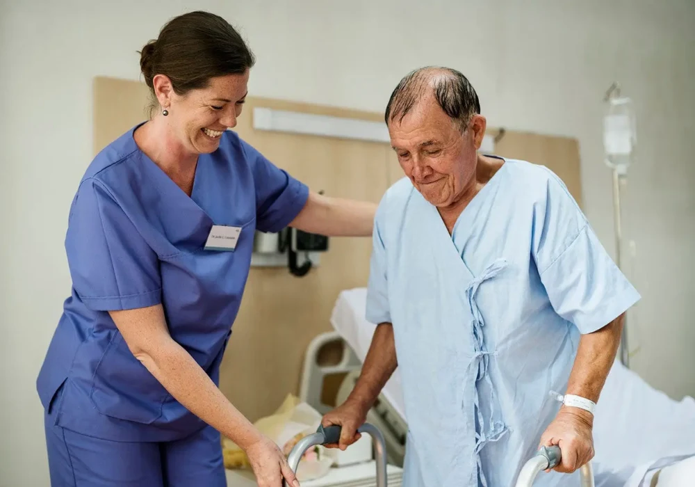 Nurse helping an older patient use a walking frame in hospital, supporting mobility care, rehabilitation and fall prevention.