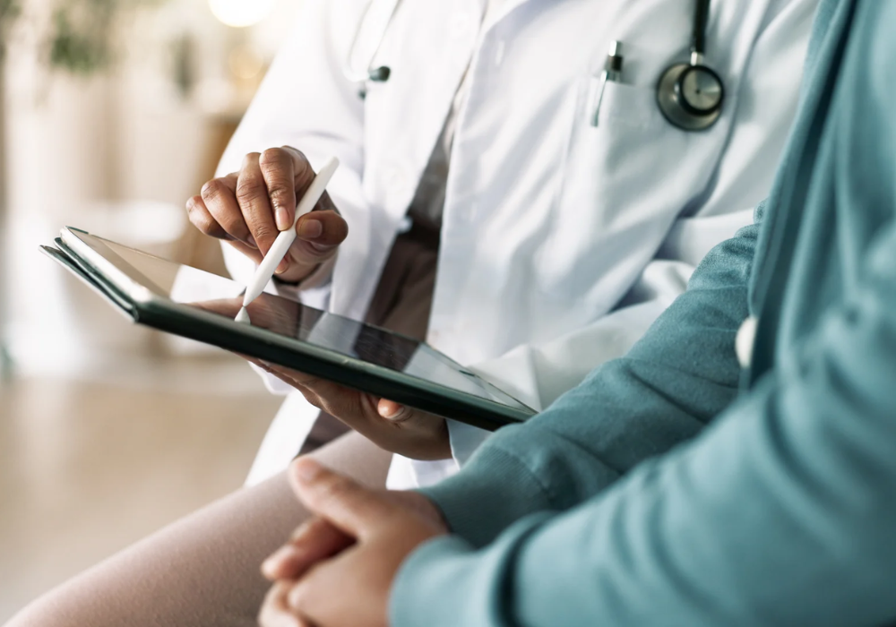 Clinician using a tablet during a patient consultation, illustrating digital documentation, shared decision-making and integration of electronic health records into routine care.
