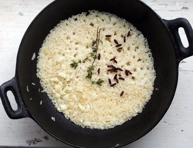 Black cast iron dish with rice, garlic and thyme