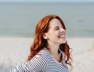 Woman with long red hair on the beach smiling with her eyes shut