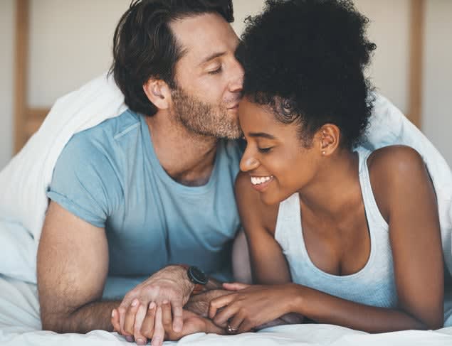 Man lying in bed with his partner kissing her affectionately on the forehead