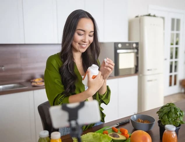 Smiling woman with long brown hair reading the label of her supplements and preparing a healthy lunch