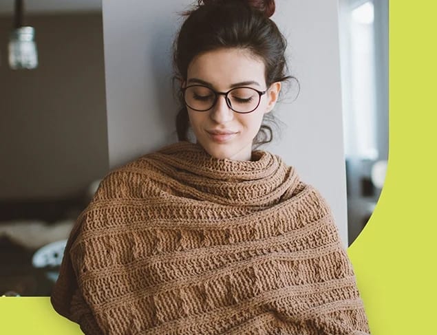 Young woman at home wrapped in a knitted shawl