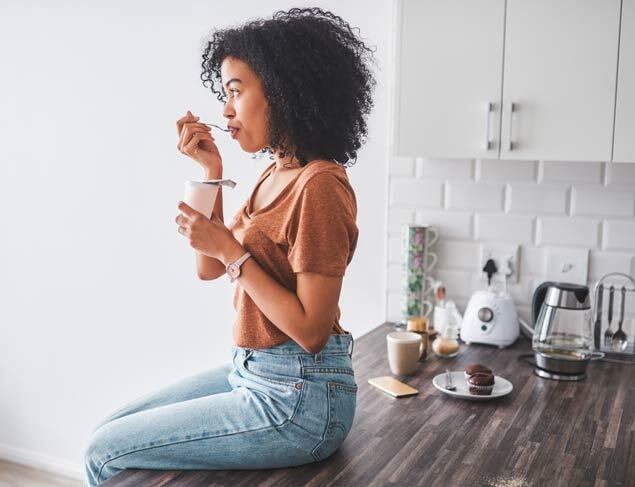 Young woman sitting on the kitchen bench eating probiotic rich yoghurt