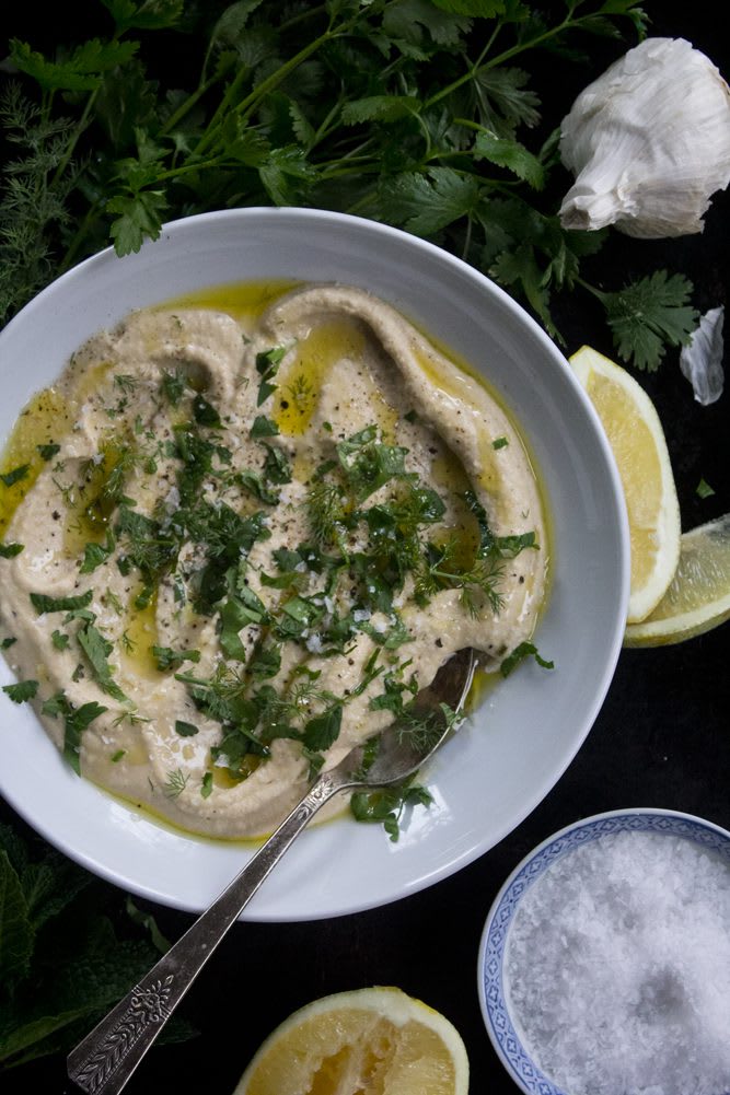 Plate of traditional hummus garnished with fresh dill, cilantro, parsley, and mint with a drizzle of extra virgin olive oil, sea salt, and fresh cracked pepper