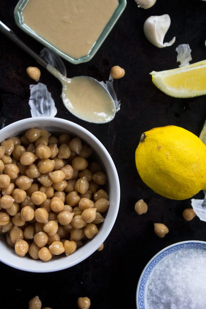 2022_TraditionalHummus_12_web Ingredients for traditional hummus: garbanzo beans in a bowl, one lemon, tahini paste, spoon, sea salt, and one garlic clove