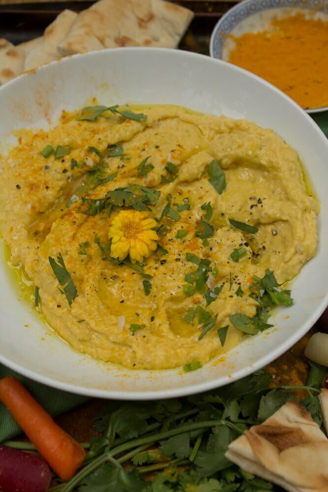 Close up view of plated mango turmeric hummus garnished with fresh cilantro and edible flower