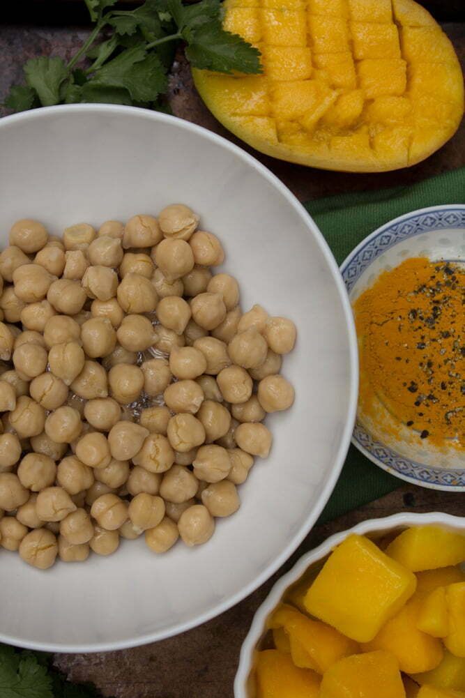 Fresh ingredients from Mango Turmeric Hummus | Bowl of chickpeas, frozen and fresh mango, turmeric with fresh cracked pepper, and cilantro