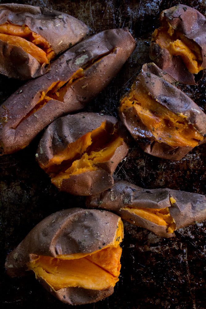 2022_RoastedSweetPotatoHummus_12web Red skinned sweet potatoes on a baking sheet sprinkled with fresh thyme, rosemary, sea salt and fresh pepper cut open to cool after roasted
