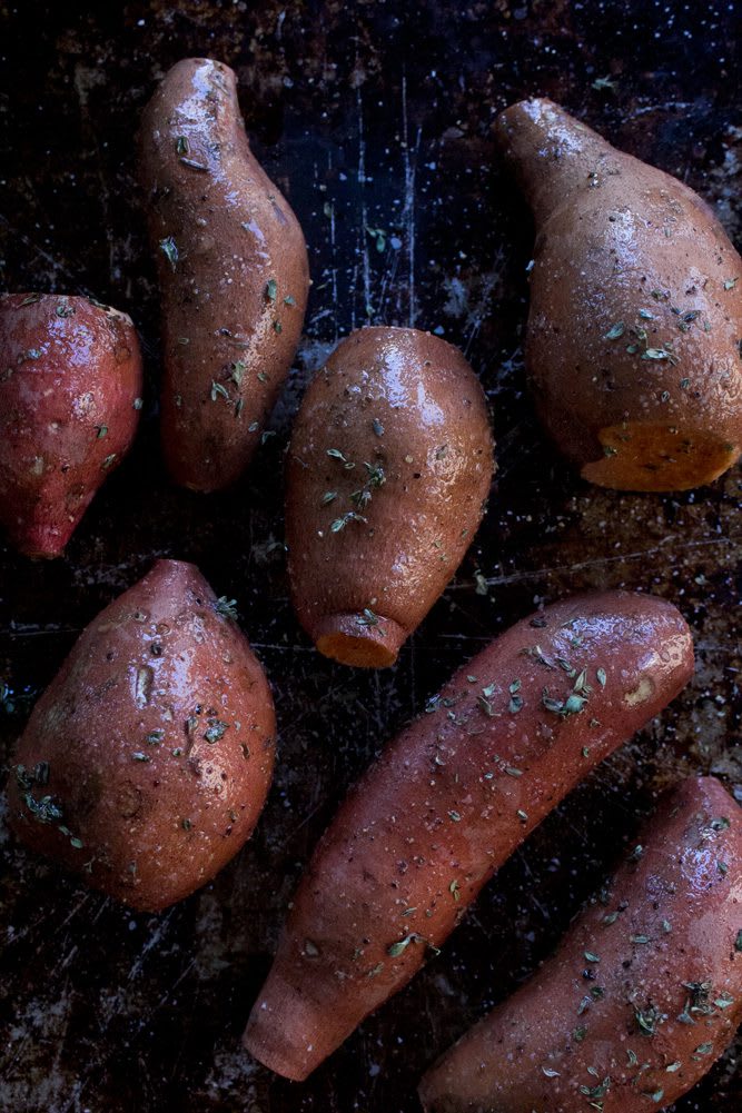 2022_RoastedSweetPotatoHummus_5web Red skinned sweet potatoes on a baking sheet sprinkled with fresh thyme, rosemary, sea salt and fresh pepper
