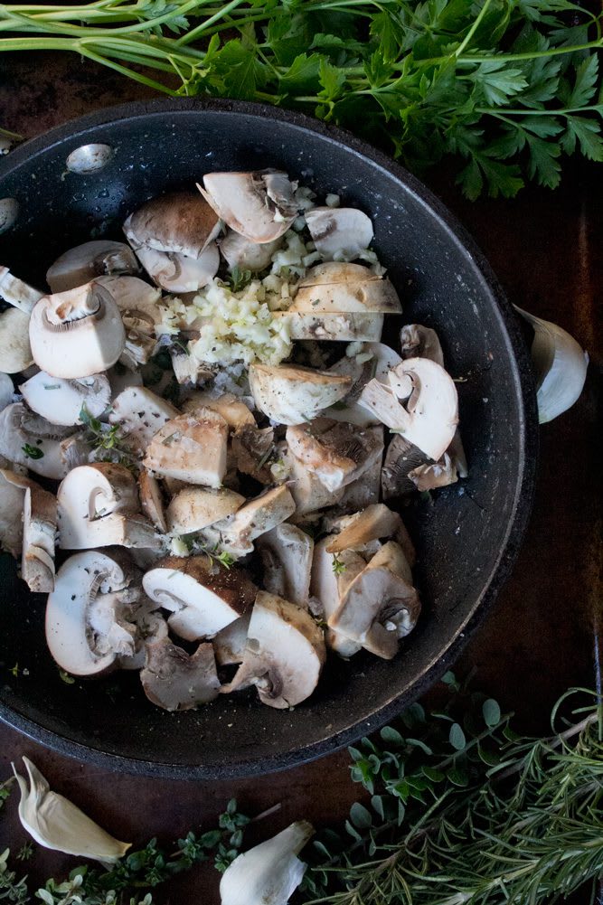 2022_MushroomThymeHummus_14_web Raw button and crimini mushrooms with garlic and herbs in a sautee pan