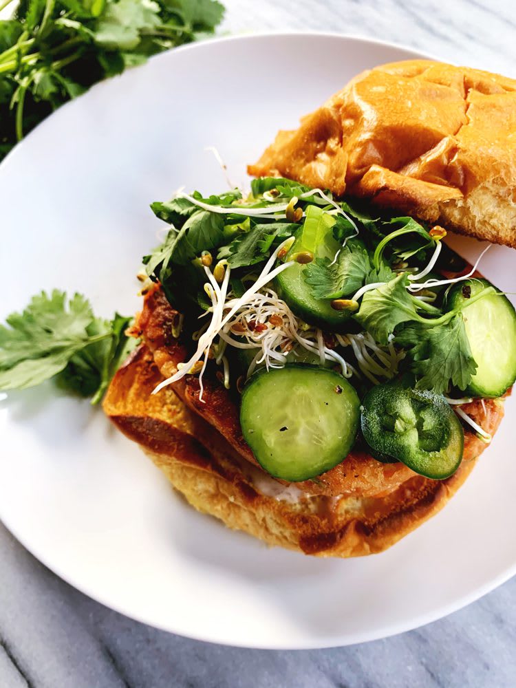 Plated Salmon Burger with pickled cucumbers, cilantro, microgreens, and jalapenos on a brioche bun