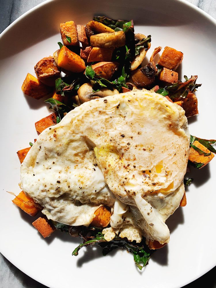 Hearty breakfast hash with diced sweet potatoes, mushrooms and kale served with a friend egg