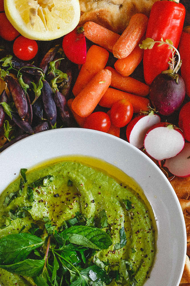 Green Goddess Hummus in shallow bowl with radishes, cherry tomatoes, flatbreads, and spring peas