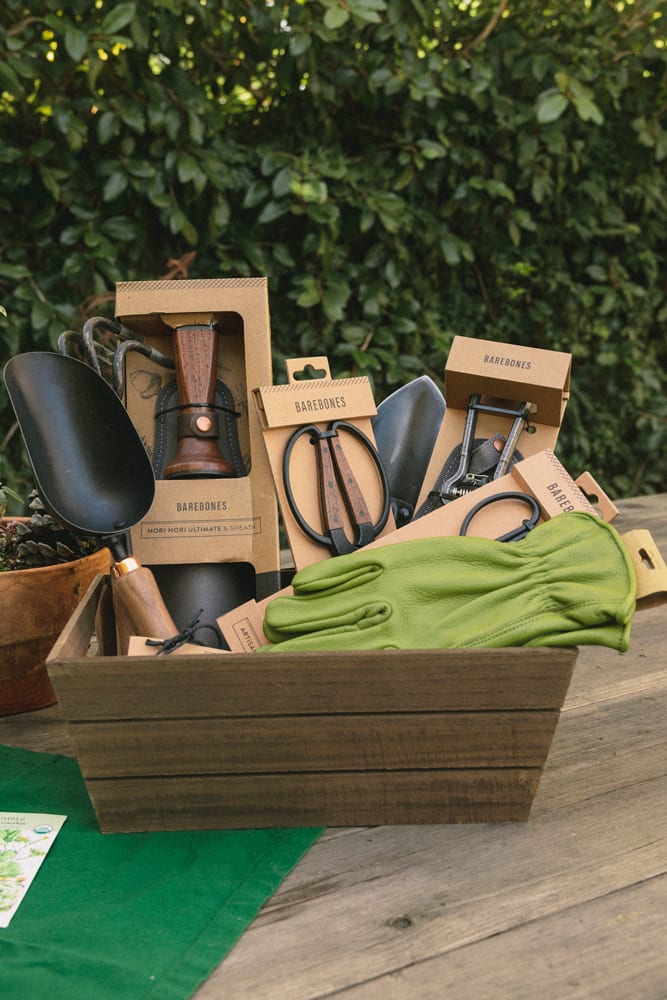 Basket full of Barebones garden tools: scoop, Hori Hori, Shears, pruner, leather gloves.