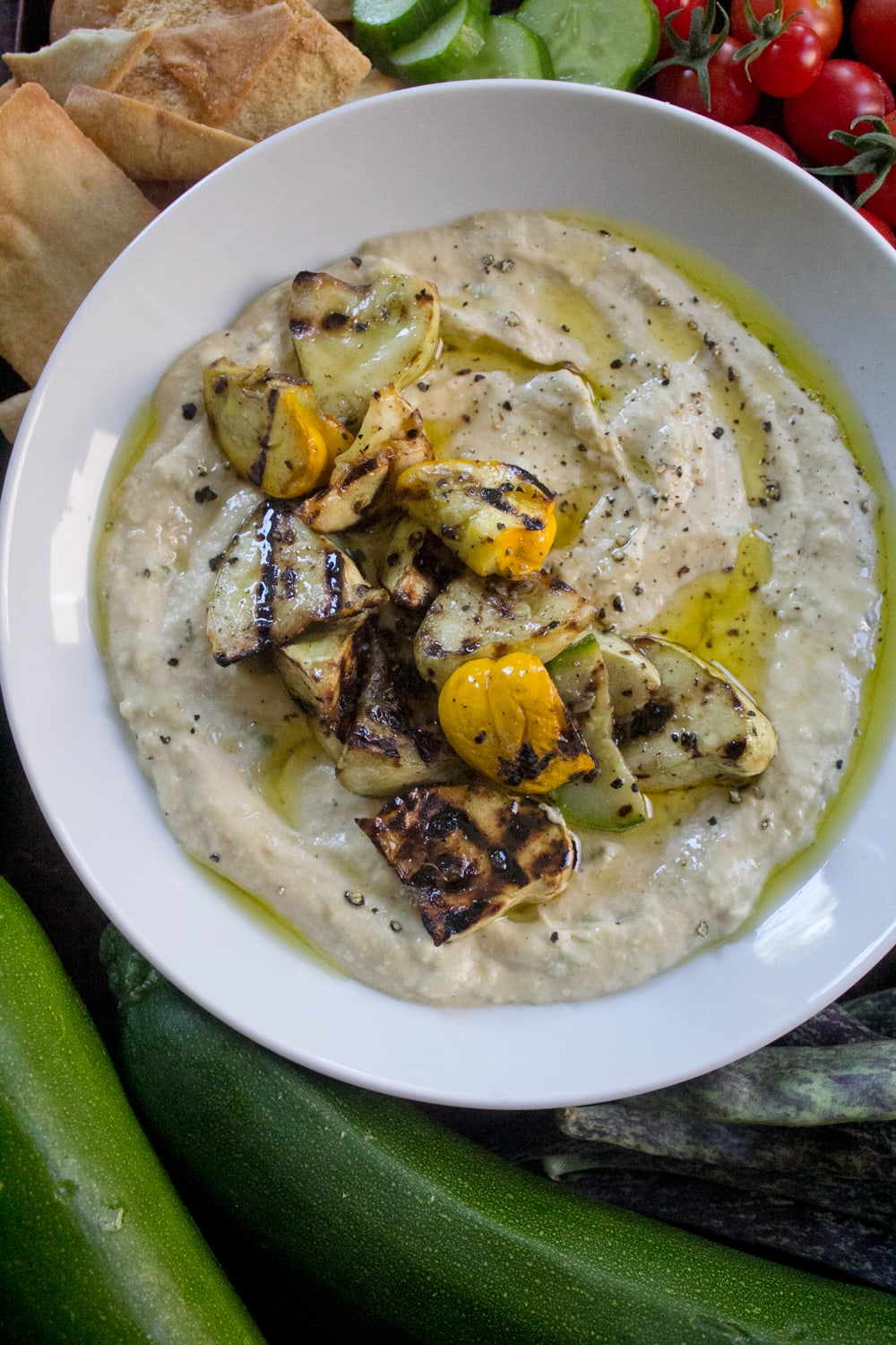 Grilled Summer Squash Hummus made with a variety of summer squashes and served with cripsy pita chips, flatbreads, cucumbers, and cherry tomatoes