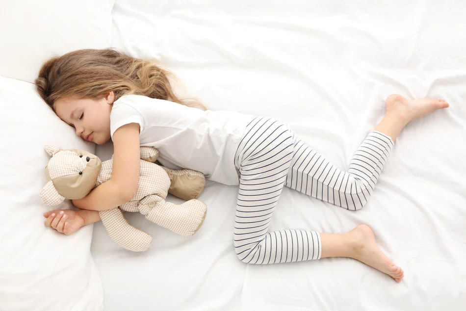 Child hugging a teddybear and napping on bed
