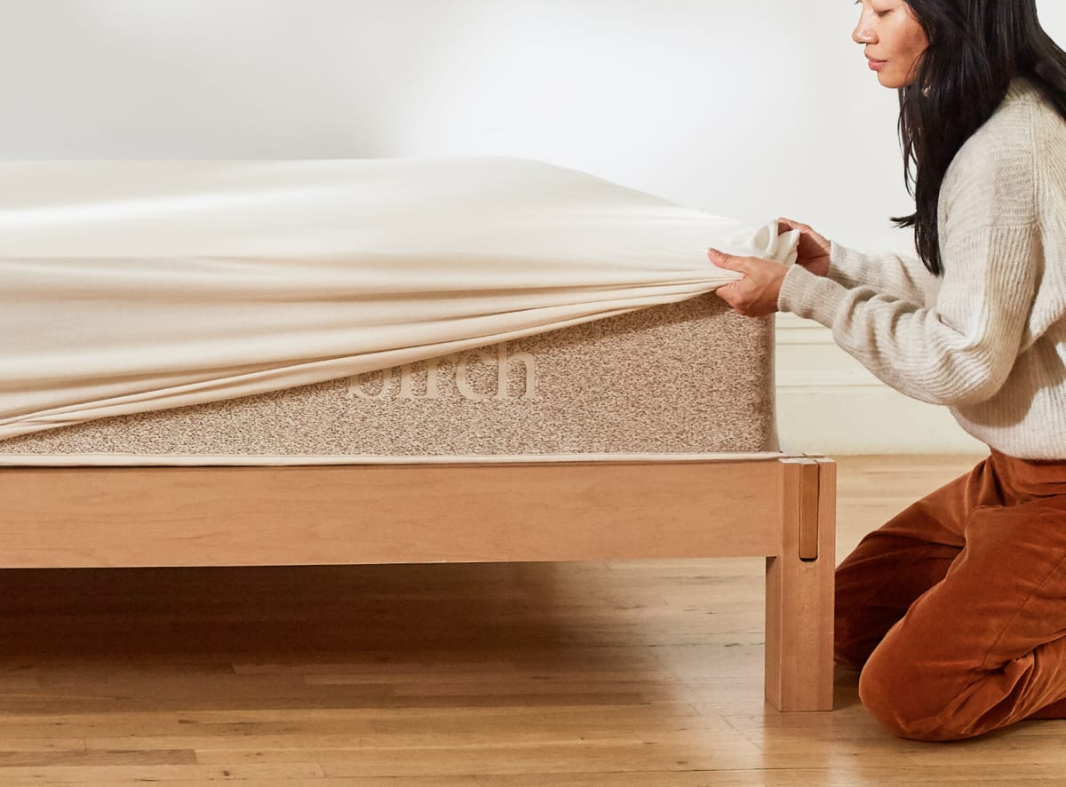 A closeup of the mattress protector being pulled over a Birch mattress