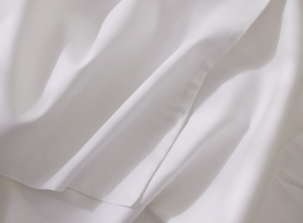 A closeup of the white sheet set on top of a mattress