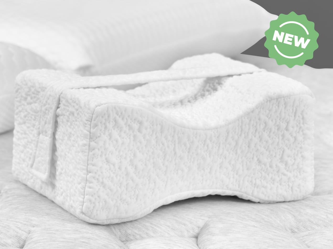 A white, contoured knee pillow with a strap is shown in a black and white image, with a green and white "NEW" badge in the upper right corner.
