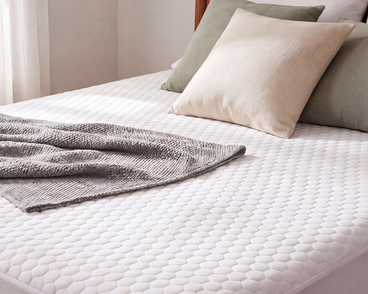 An image of the GlacioTex Cooling Mattress Protector on a bed in a bedroom scene