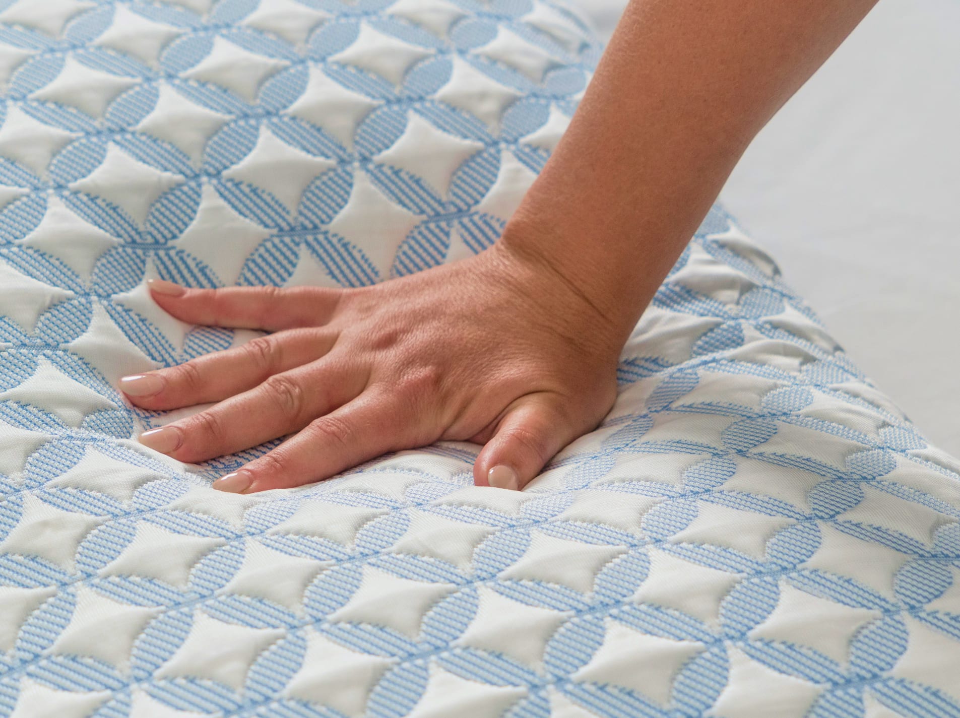 A hand presses into the pillow, highlighting the plush, quilted texture and the soft feel of the fill.