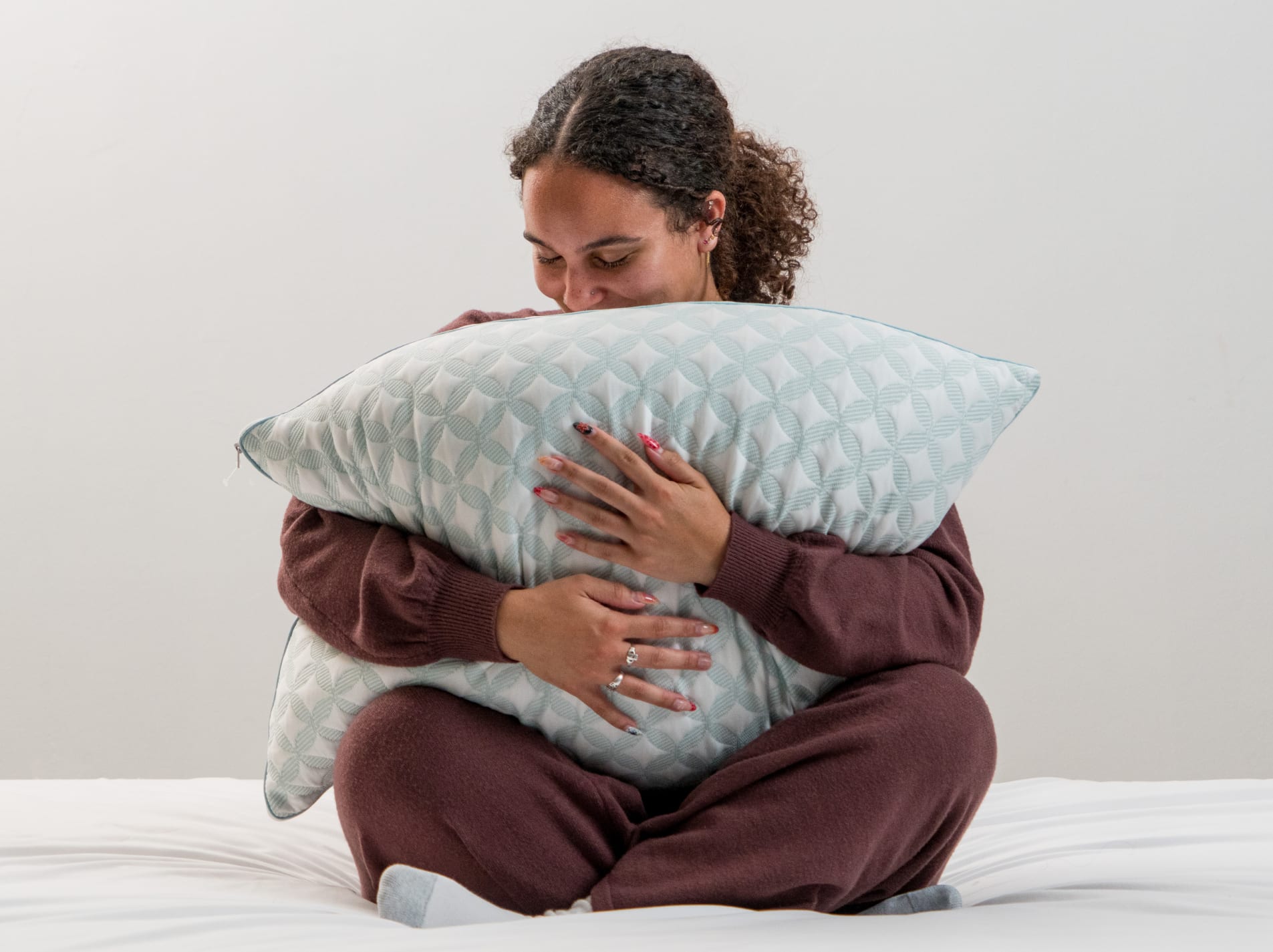 A woman is sitting on a bed, happily hugging a pillow to her chest.