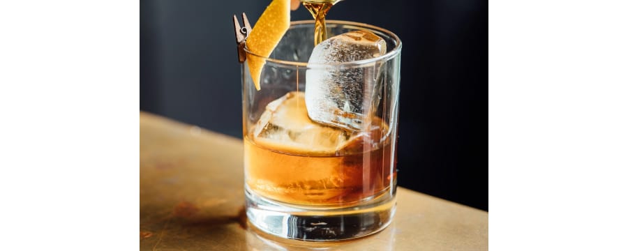 Whiskey sour in glass with an icecube and orange rind