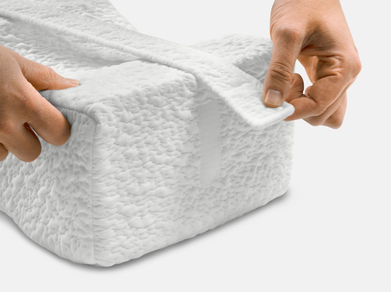 A person's hands are shown adjusting the strap on a white, textured knee pillow.