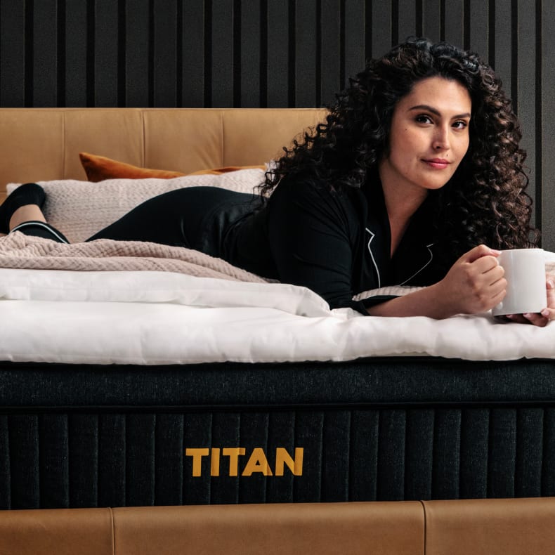 Woman lounging with a mug on the Titan Plus Luxe mattress in a modern bedroom setting.