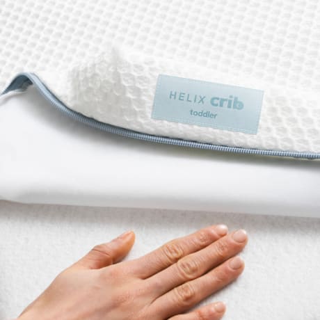 An image of the Helix Crib Cover with a hand placing across the bottom