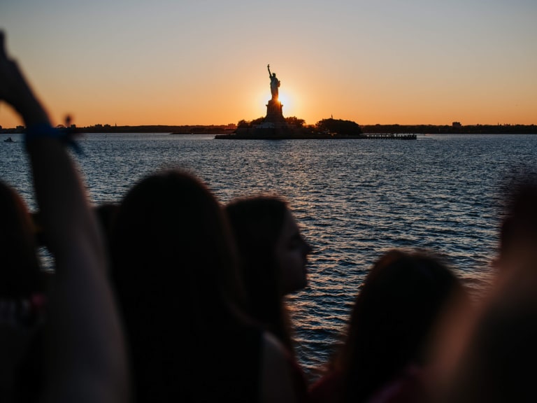 El sol poniéndose detrás de la Estatua de la Libertad, visto desde el ferry | ©Hellotickets