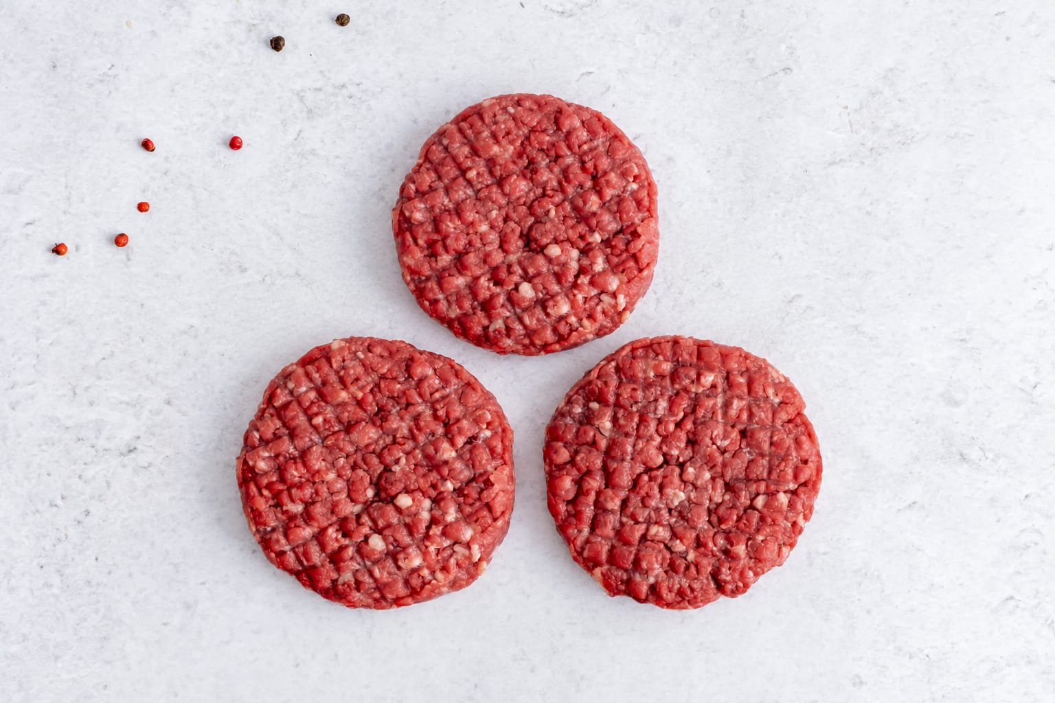 Three grass fed beef burger patties, raw, on light marble