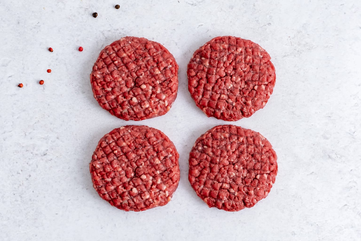 Four grass fed beef burger patties, raw, on light marble