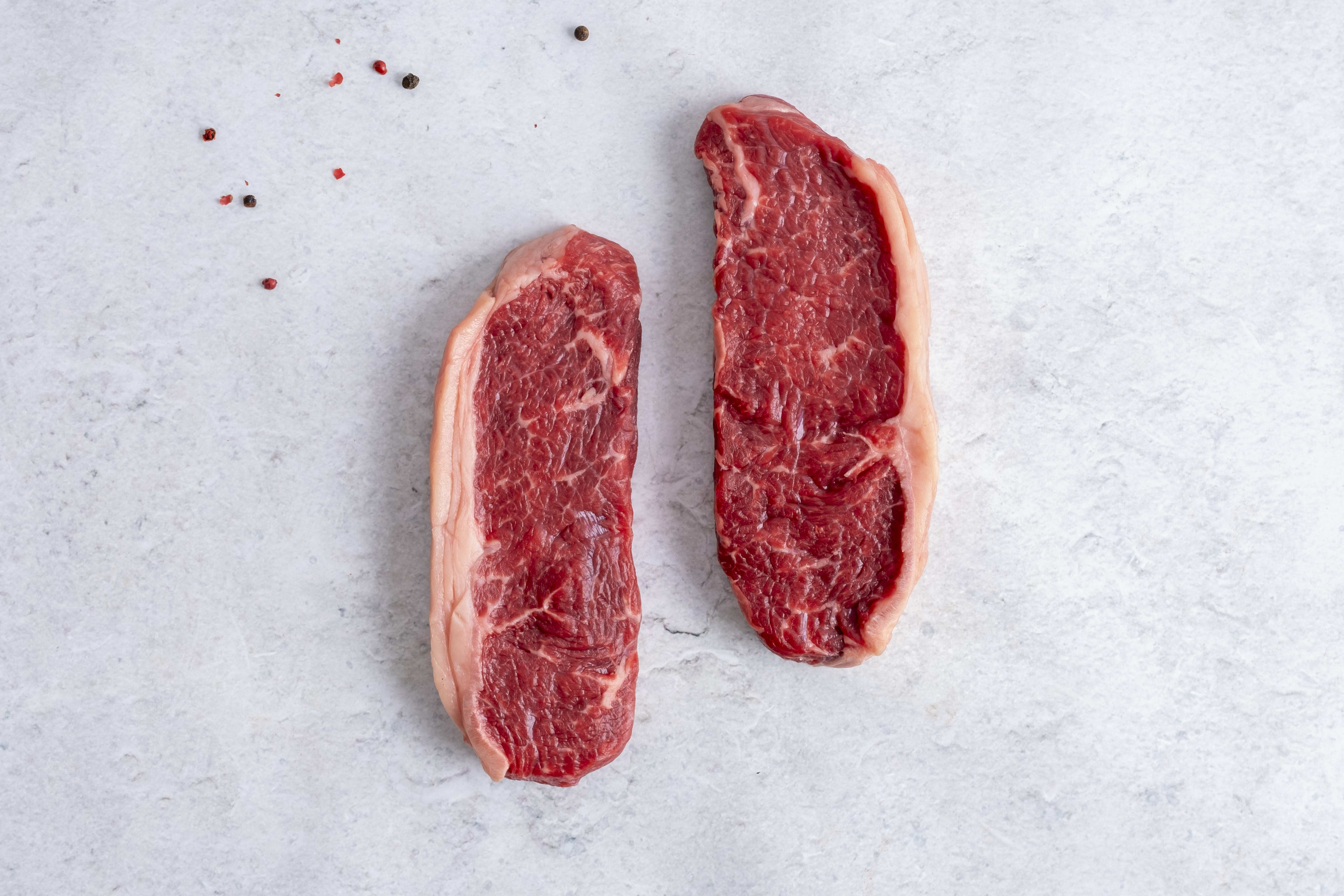 Two grass fed sirloin steaks, raw, on light marble