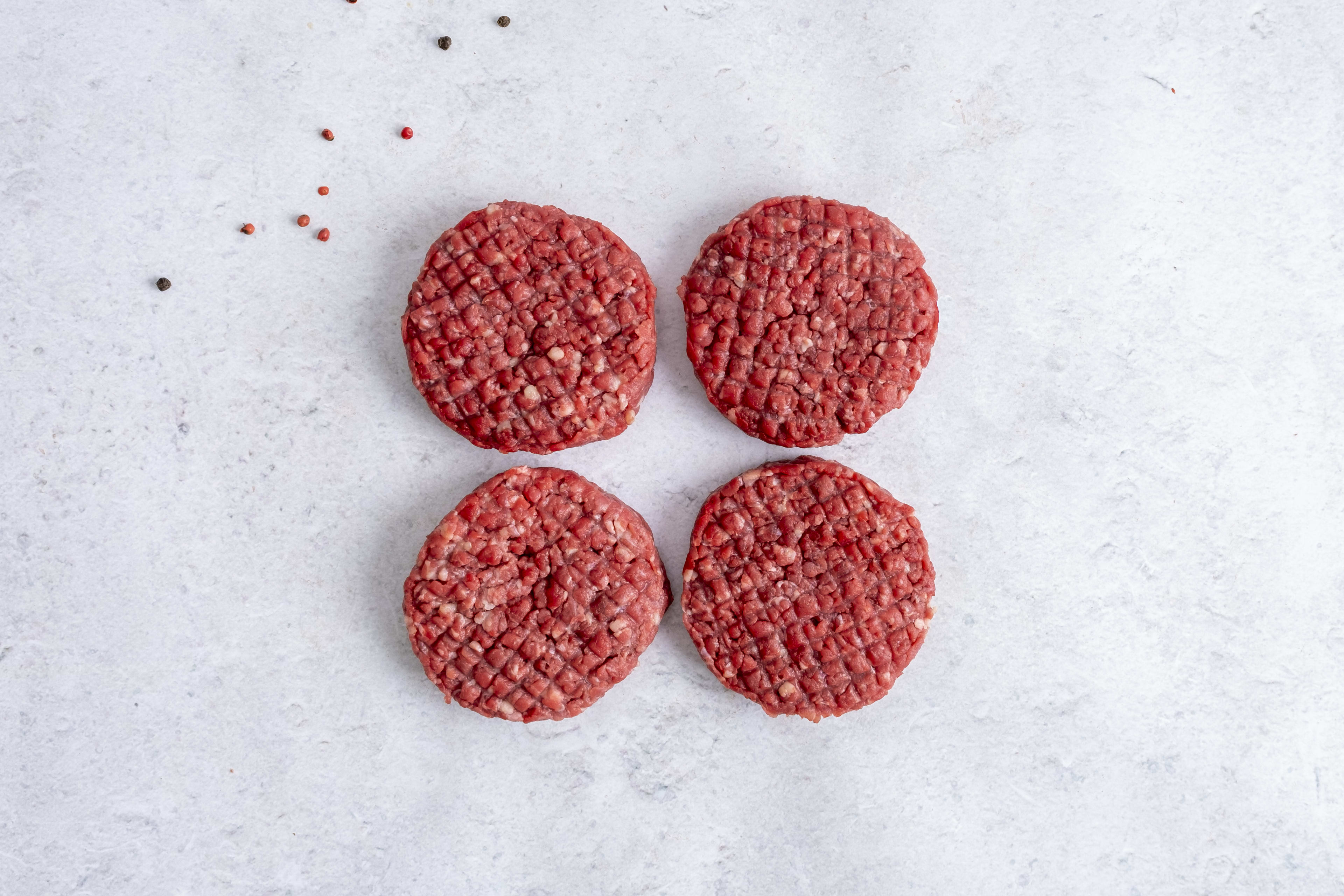 Four grass fed beef burger patties, raw, on light marble