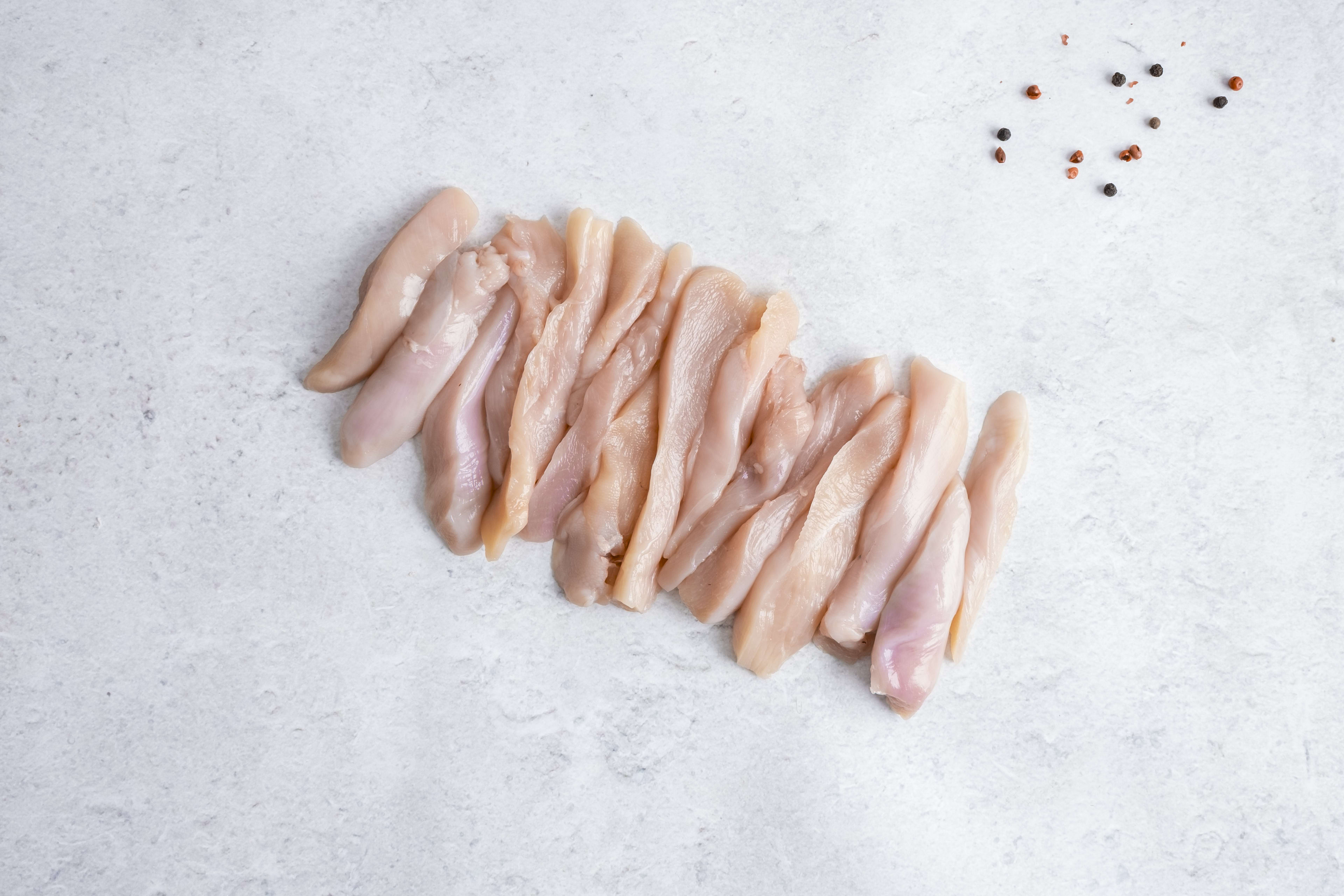 Chicken breast strips, raw, on light marble