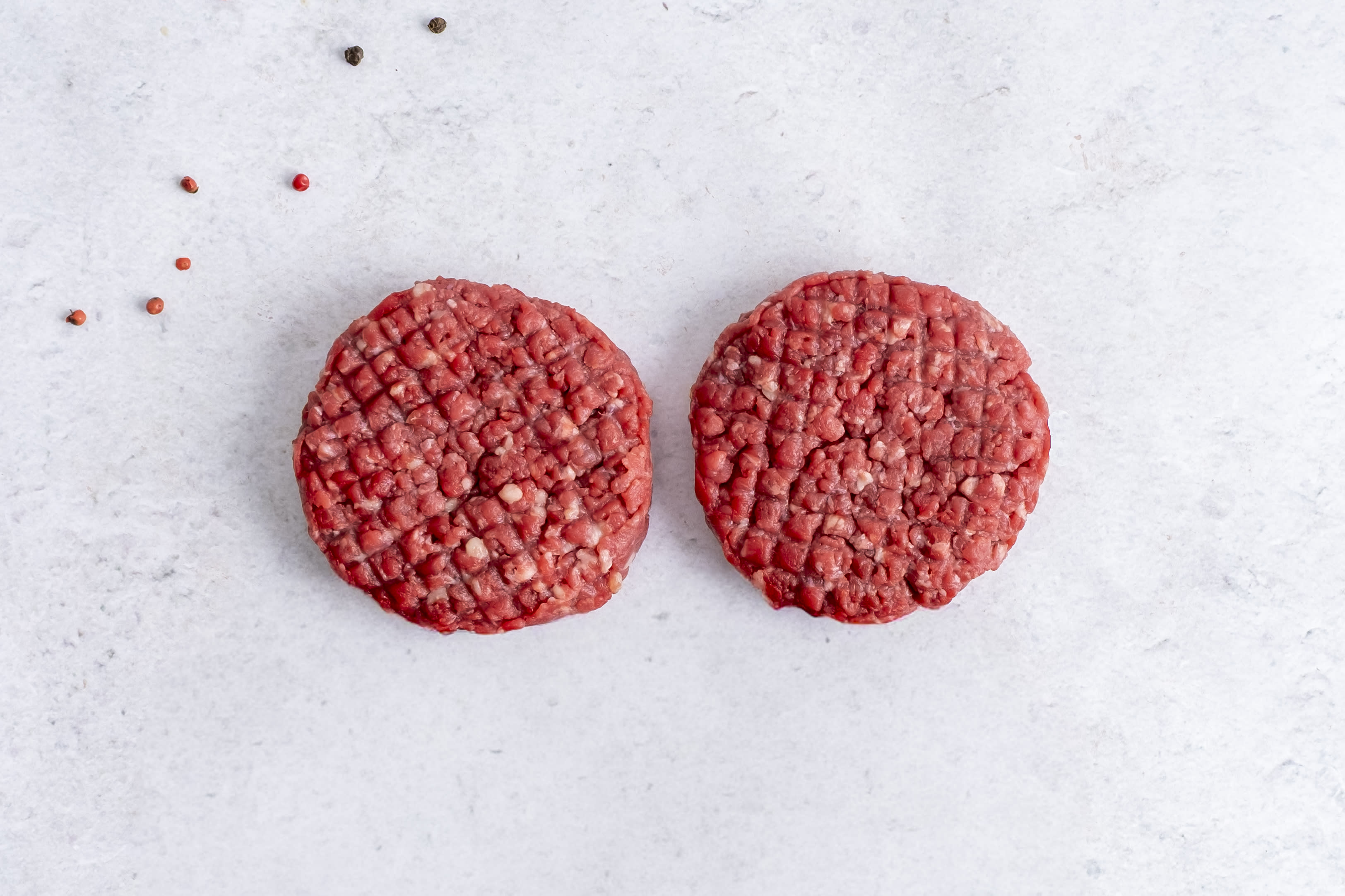 Two grass fed beef burger patties, raw, on light marble