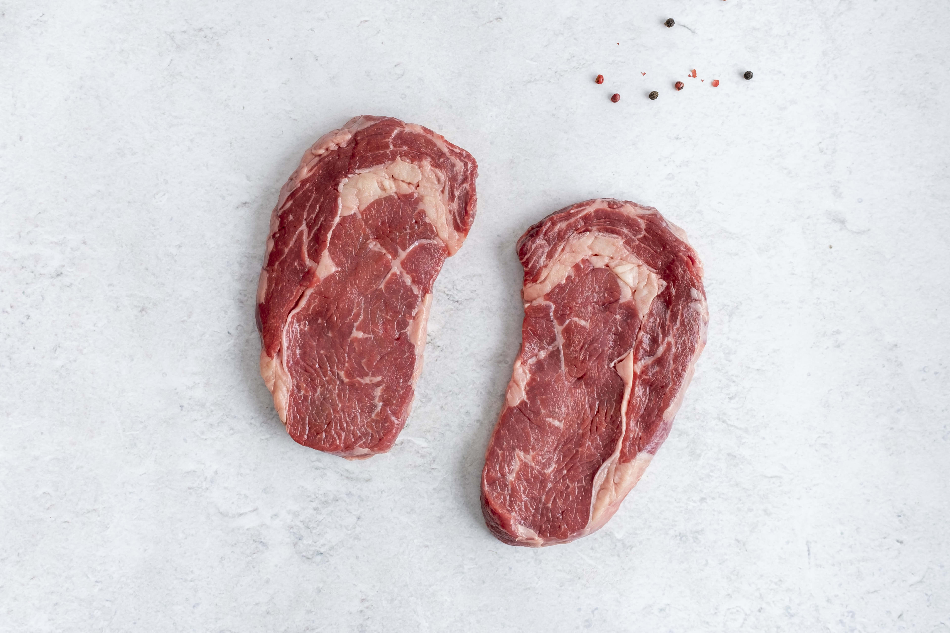 Two grass fed ribeye steaks, raw, on light marble