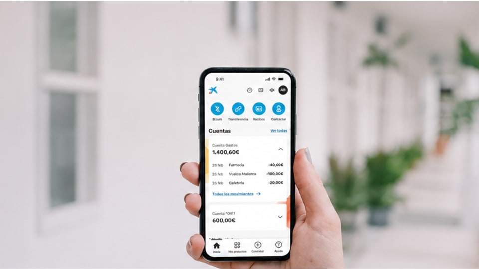 Una mano que sostiene un smartphone en el que se ve una aplicación bancaria con los saldos de las cuentas y las transacciones recientes.